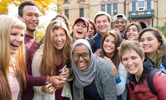 A group of smiling, laughing Hamline students gathered in front of Old Main and leaning together for the picture