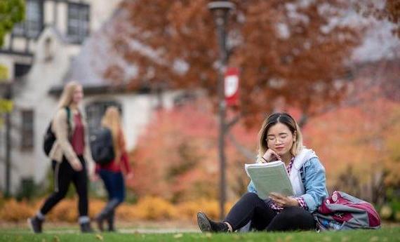 International undergrad student on campus reading a notebook.
