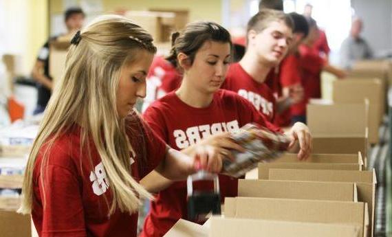 Three Hamline student wearing red "PIPERS" shirts taping cardboard boxes while volunteering