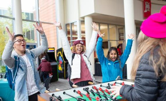 A few students cheer near a foosball table that they're playing on
