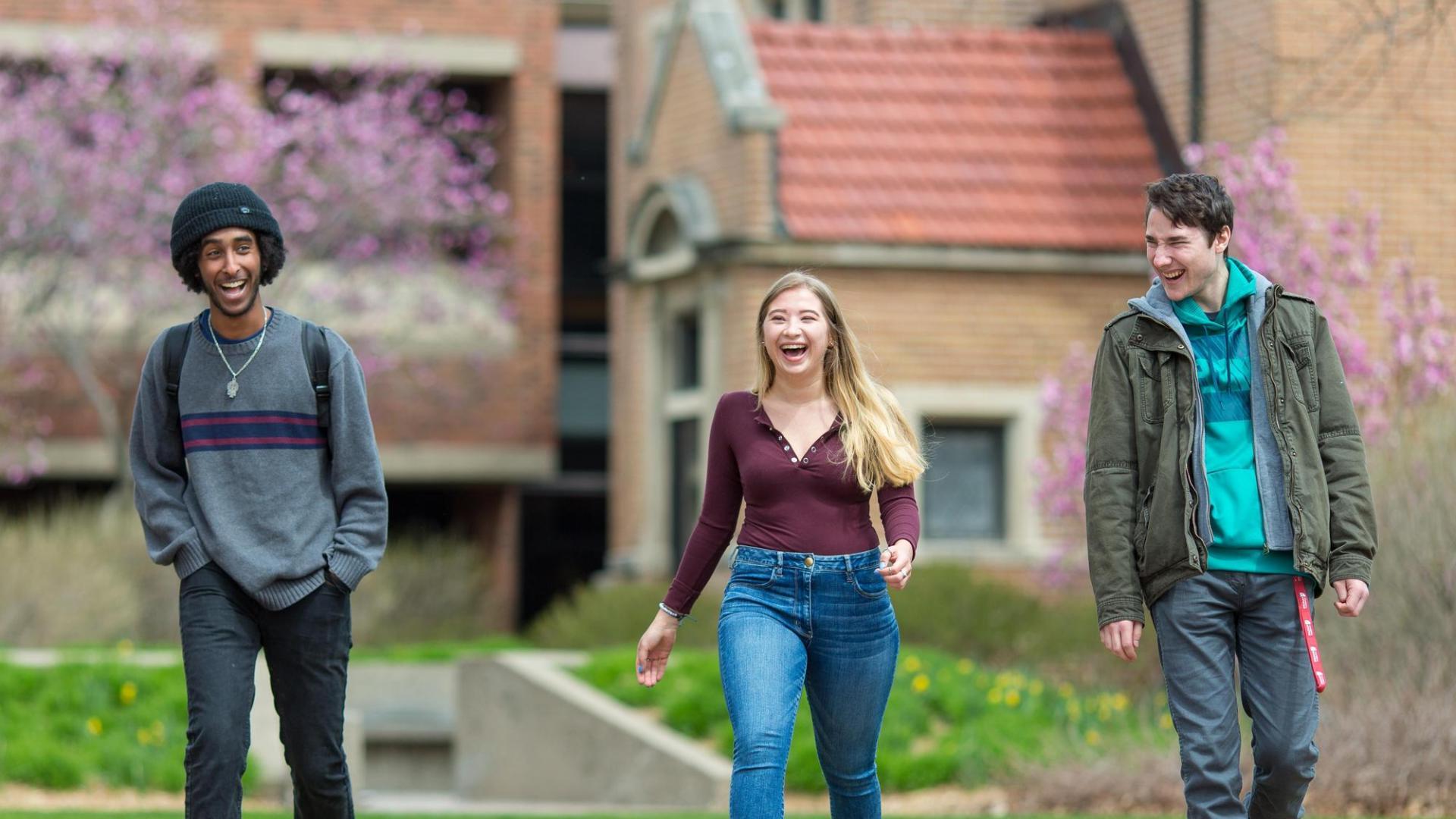 three students walking on Hamline University campus in spring, with flowering trees